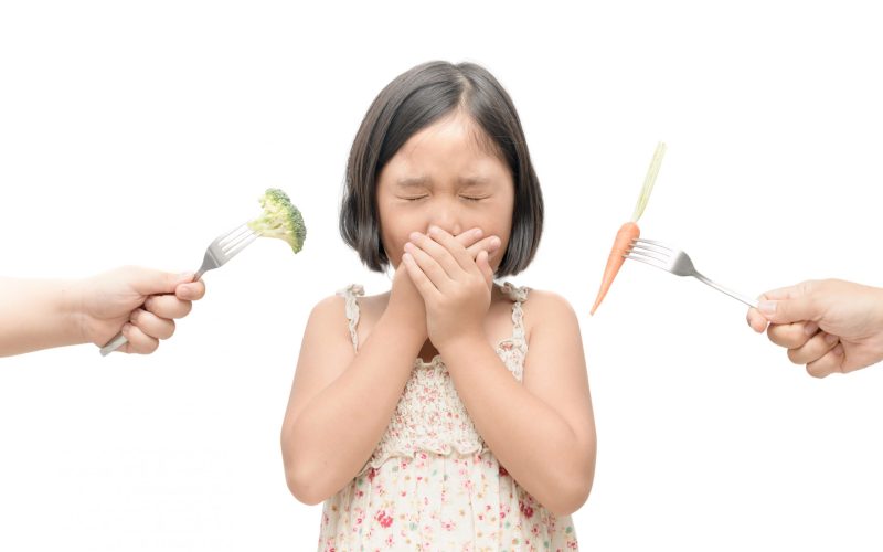 child girl with expression of disgust against vegetables isolated on white background